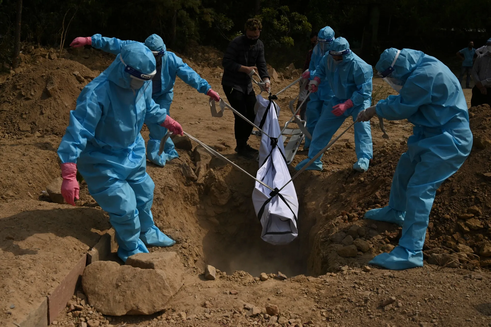 Relatives wearing personal protective equipment lower the body of a Covid-19 coronavirus victim during a burial in New Delhi on April 30.