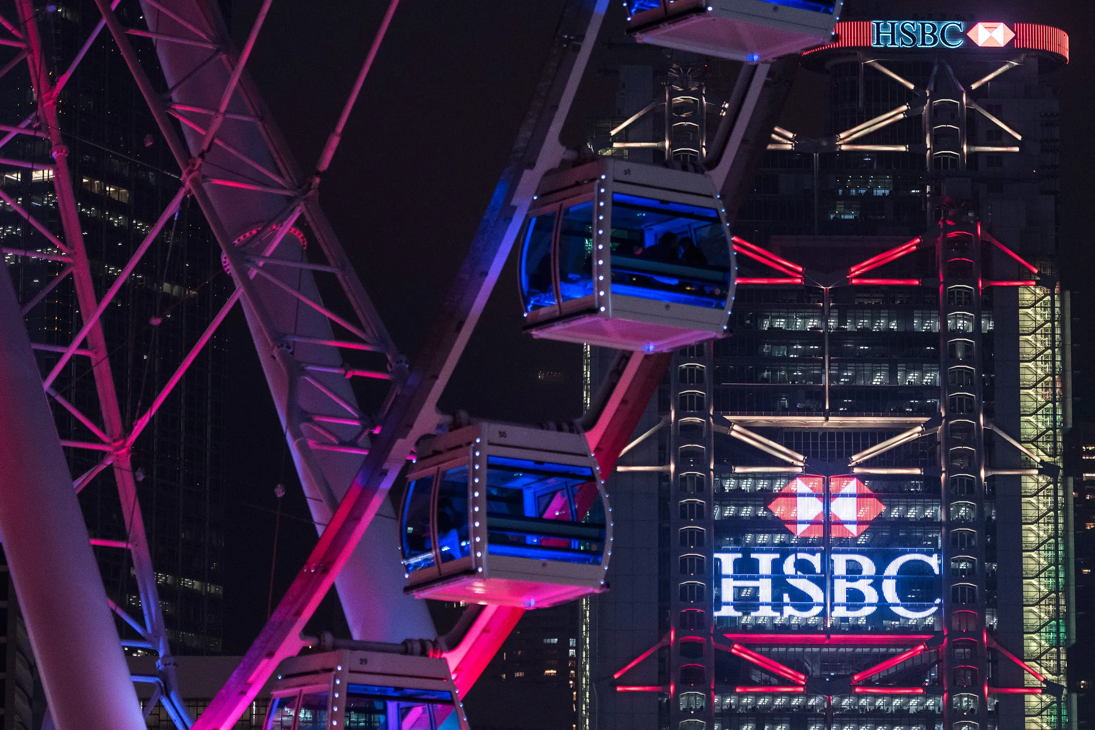 The HSBC Holdings Plc headquarters building stands behind the Hong Kong Observation Wheel at night in Hong Kong.
