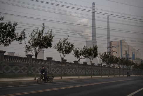 A Chinese man rides a bicylce as a coal fired power plant is seen in the background. Photographer: Kevin Frayer/Getty Images