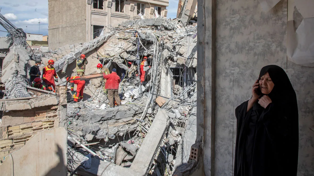 A woman speaks on the phone as emergency workers sift through rubble of a residential building that was hit in an airstrike in the early hours of March 27 in Tehran.