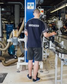 A worker smooths the joint of strap and footbed before application of the sole.