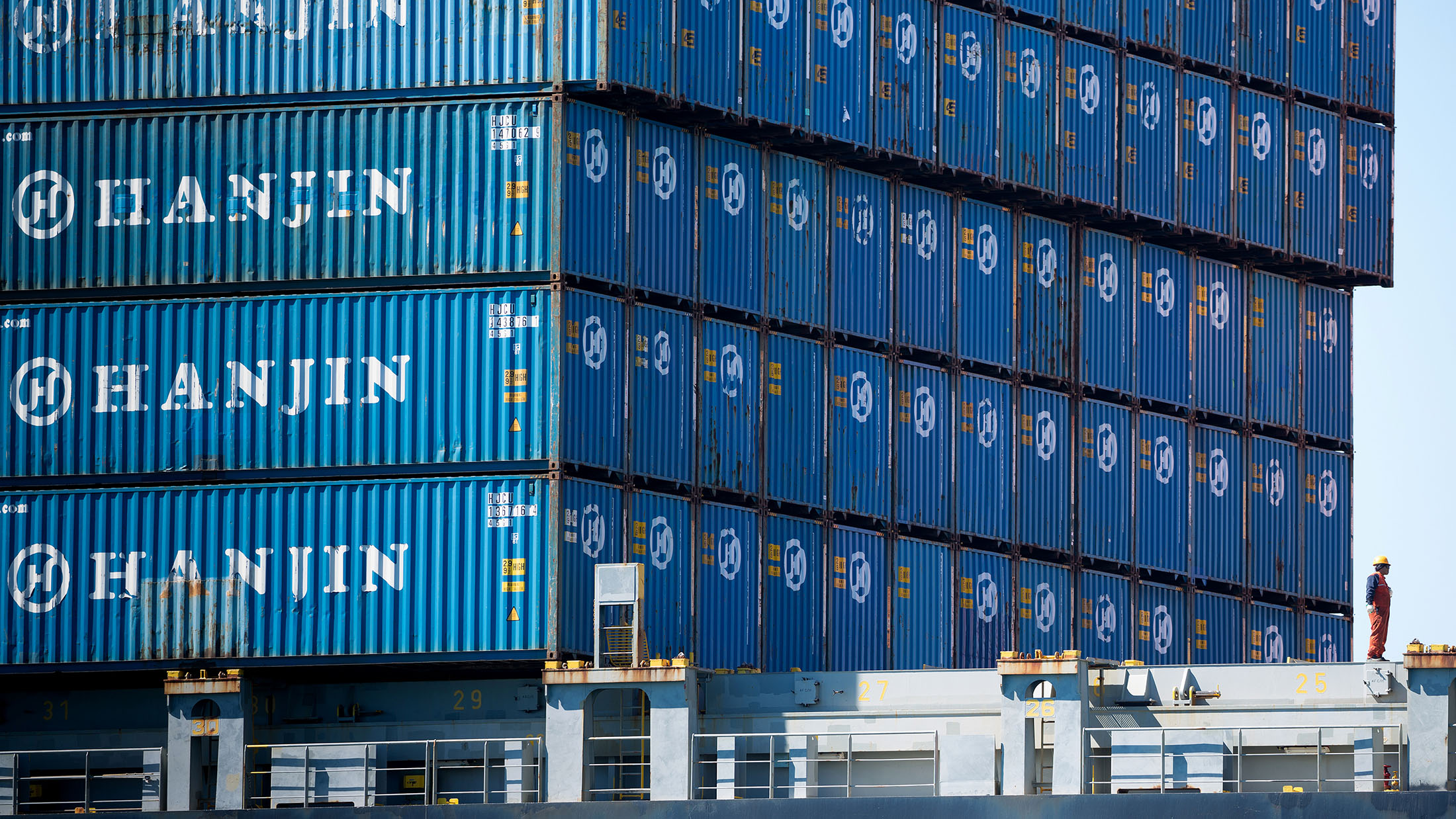 A worker stands as containers sit stacked on the Hanjin Gdynia cargo ship berthed at the Port of Long Beach in Long Beach, California, U.S., on Thursday, Sept. 15, 2016. Bankrupt Hanjin Shipping Co.'s efforts to unload vessels in the U.S. while it goes through bankruptcy in South Korea are meeting with complaints from cargo owners and from the companies that service and equip its fleet.
