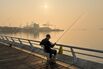 Man Fishing On Seafront Boardwalk With Yantian Port In Background In Shenzhen