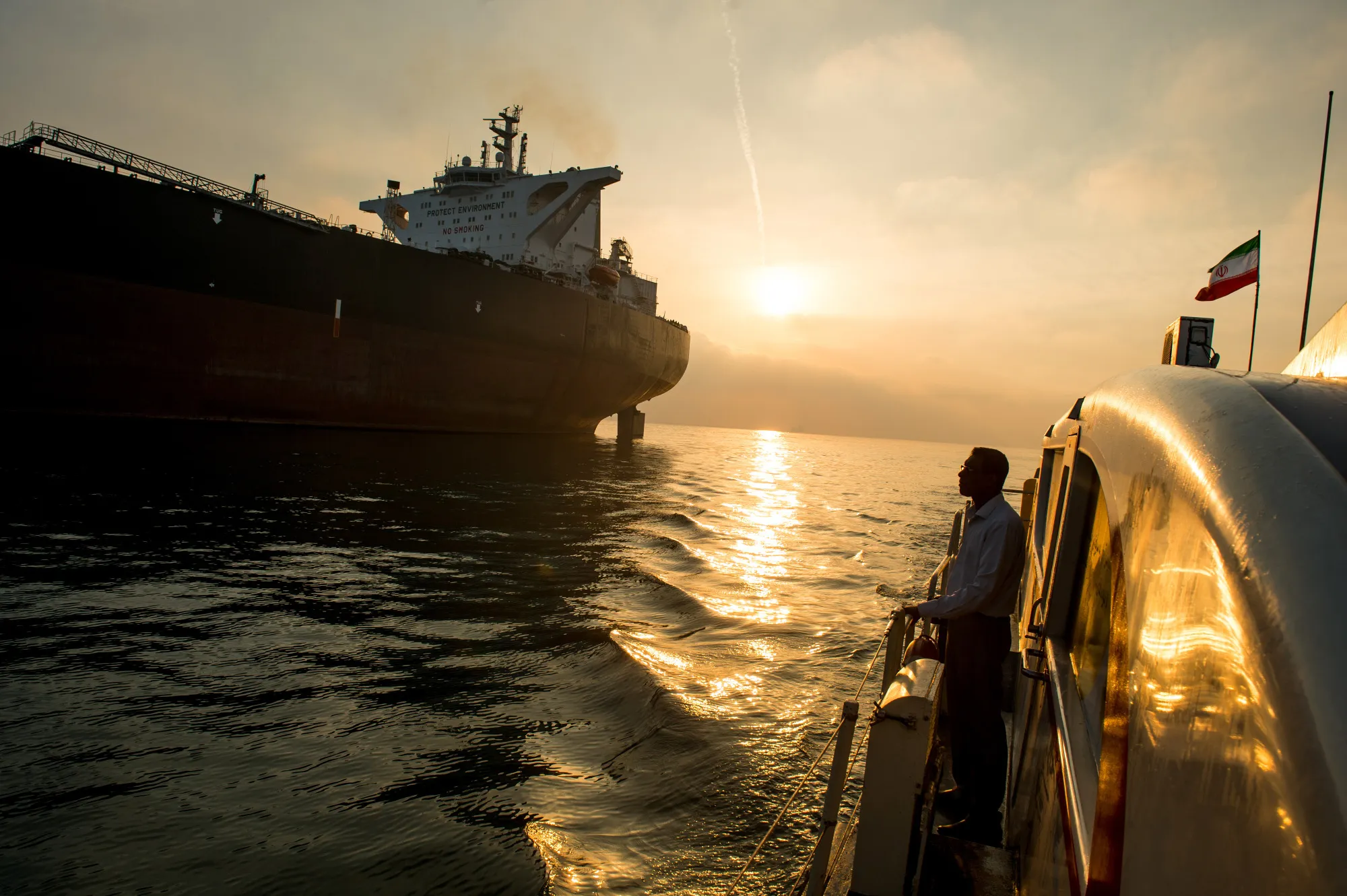 A support vessel flying an Iranian national flag sails alongside the oil tanker 'Devon' as it prepares to transport crude oil to export markets.