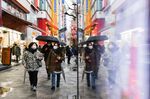 Pedestrians wearing protective masks and holding umbrellas walk in the Akihabara shopping district of Tokyo, Japan.