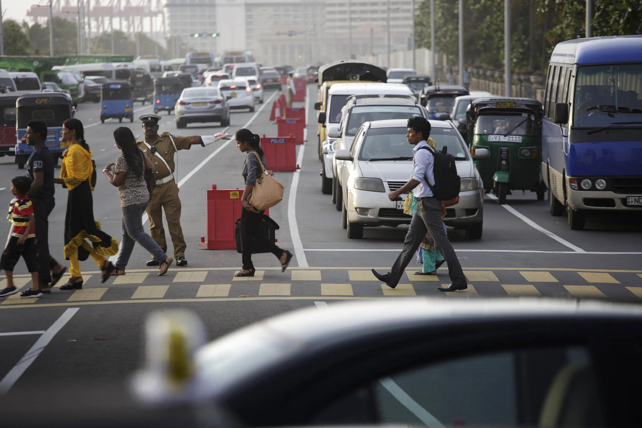Pedestrians cross a road as a police officer directs traffic during the morning rush hour in Colombo, Sri Lanka, on Tuesday, July 21, 2015. The Central Bank of Sri Lanka kept its interest rates unchanged and said near-record-low inflation is likely to continue for the next few months as the country prepares for its parliamentary elections due Aug. 17.
