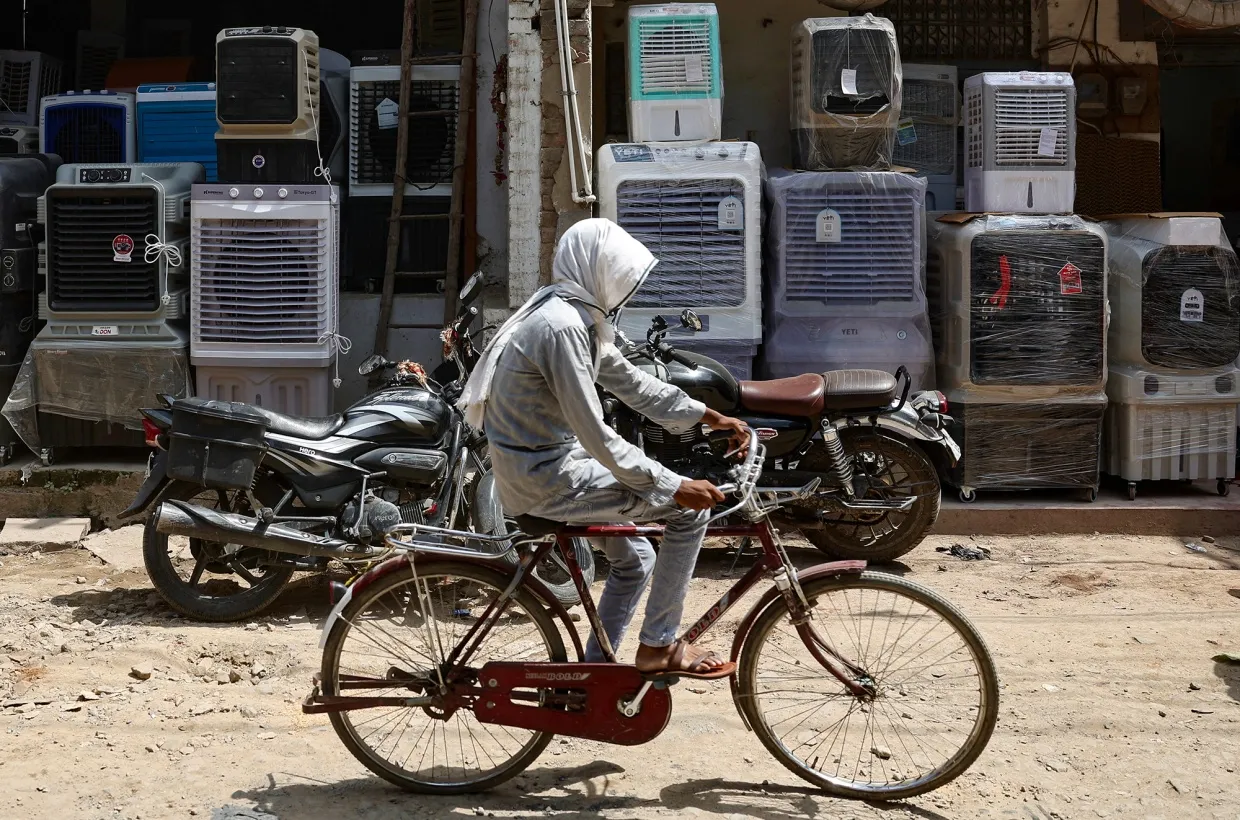 A man with his face covered with a cloth rides a bicycle past air coolers outside a shop on a hot day in Varanasi, India on May 18.