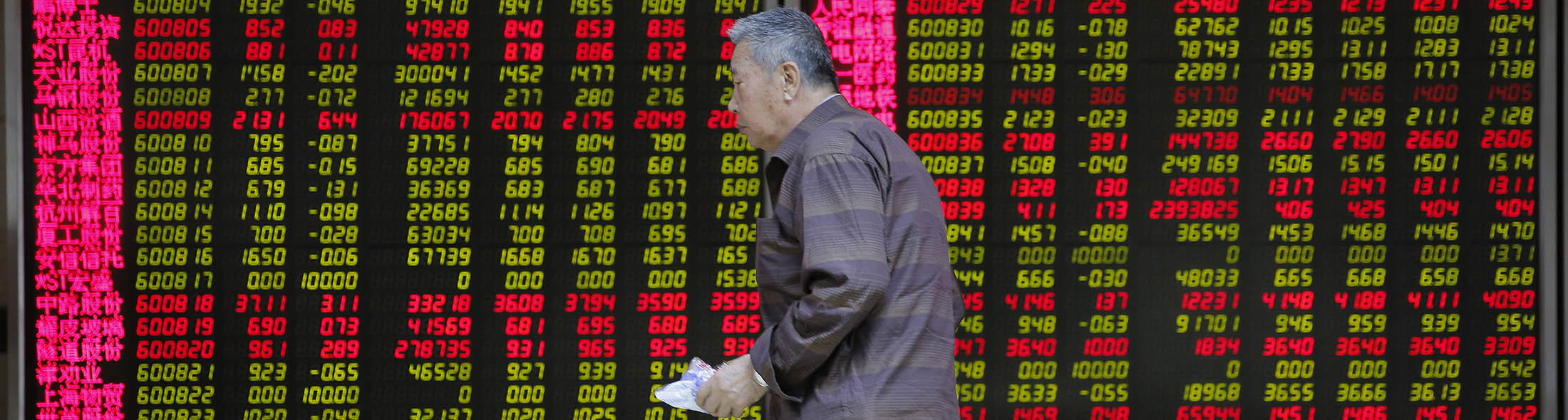 A Chinese investor walks past large screens displaying share prices at a securities brokerage house in Beijing, China.
