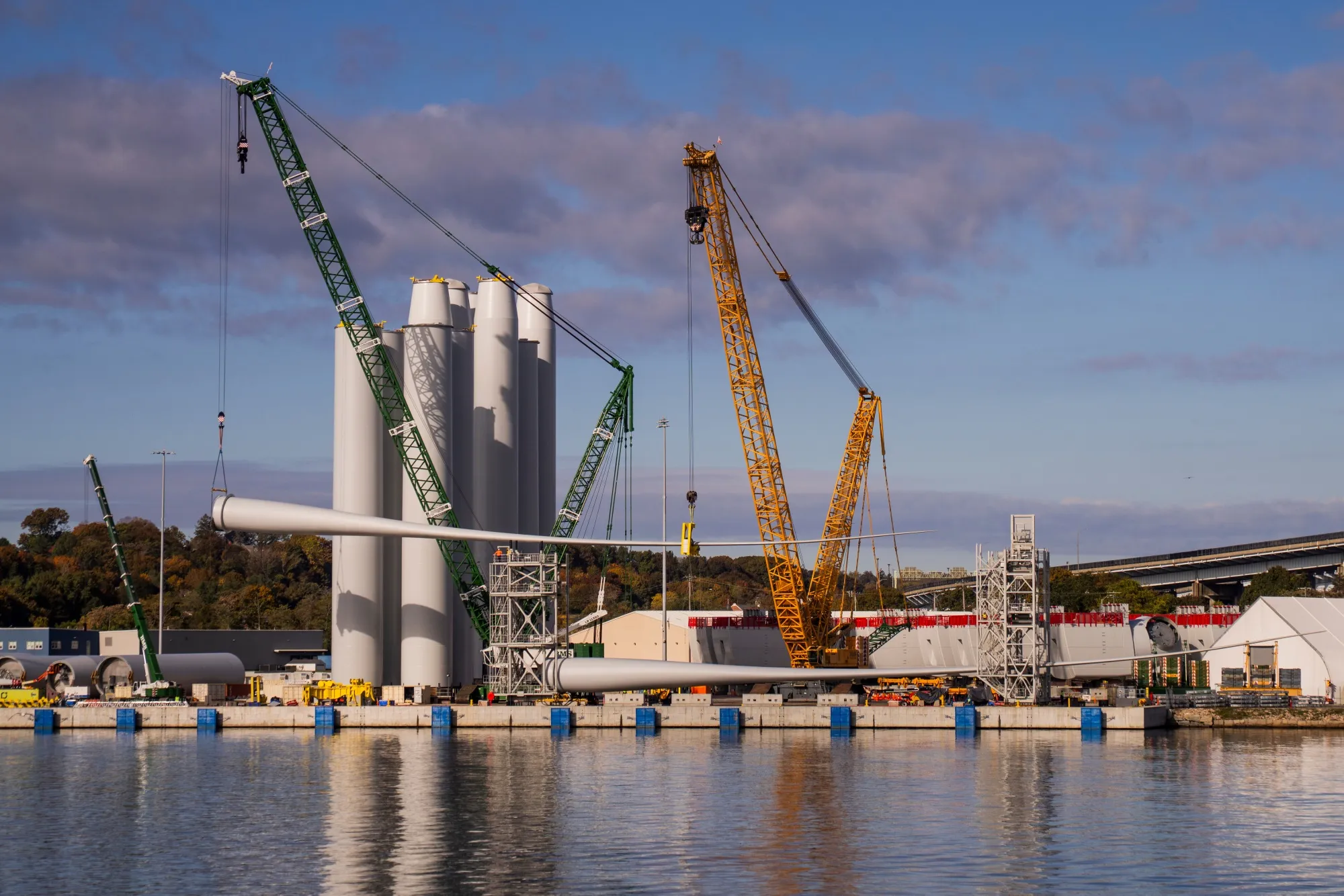 A turbine blade is lifted onto a rack near tower sections at the Revolution Wind project assembly site at State Pier in New London, Connecticut on Oct. 24.&nbsp;