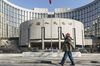 A pedestrian wearing a protective mask walks past the People's Bank of China (PBOC) building in Beijing, China, on Tuesday, March 17, 2020. China suffered an even deeper slump than analysts feared at the start of the year as the coronavirus shuttered factories, shops and restaurants across the nation, underscoring the fallout now facing the global economy as the virus spreads around the world.