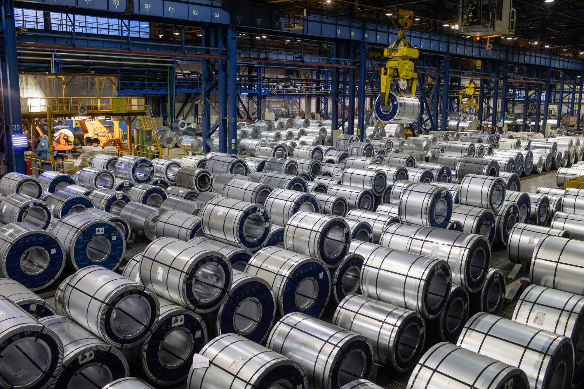 Rolls of zinc-coated steel sheet are stacked by crane in a storage area at a steel mill in Russia.