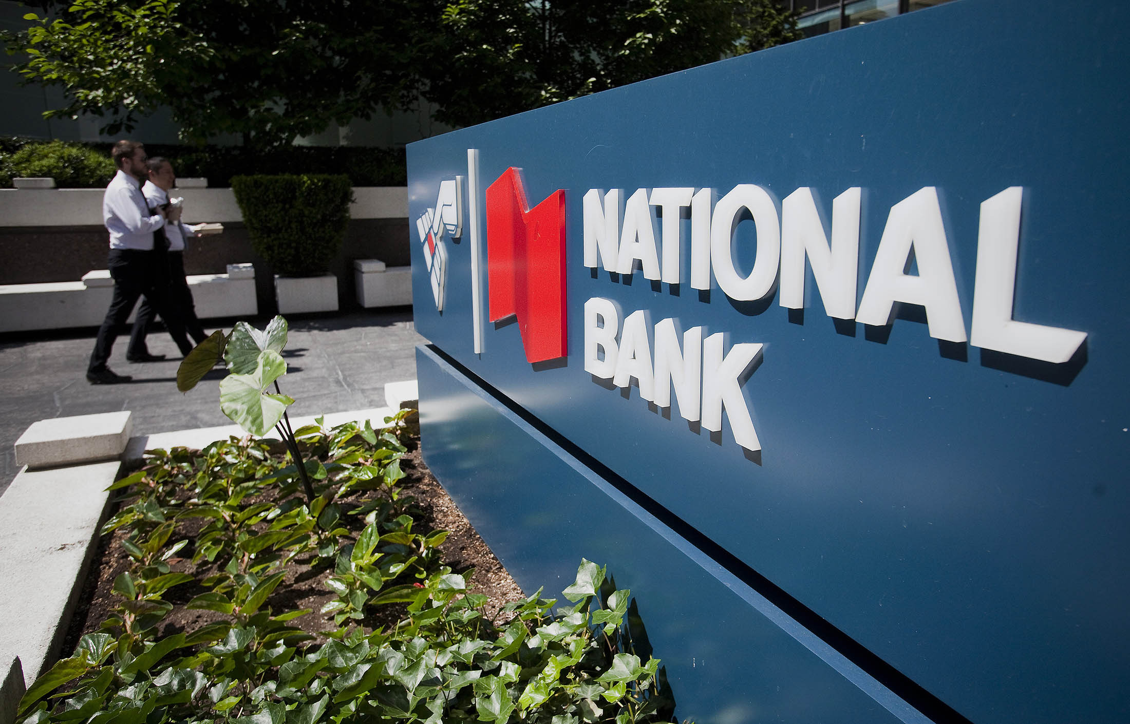 Pedestrians walk past National Bank of Canada signage in downtown Vancouver, British Columbia, Canada, on Thursday, Monday, May 28, 2015. National Bank, Canada's sixth-largest lender, reported a 12 percent increase in net income to C$404 million and raised its dividend 4 percent to 52 cents a share.

