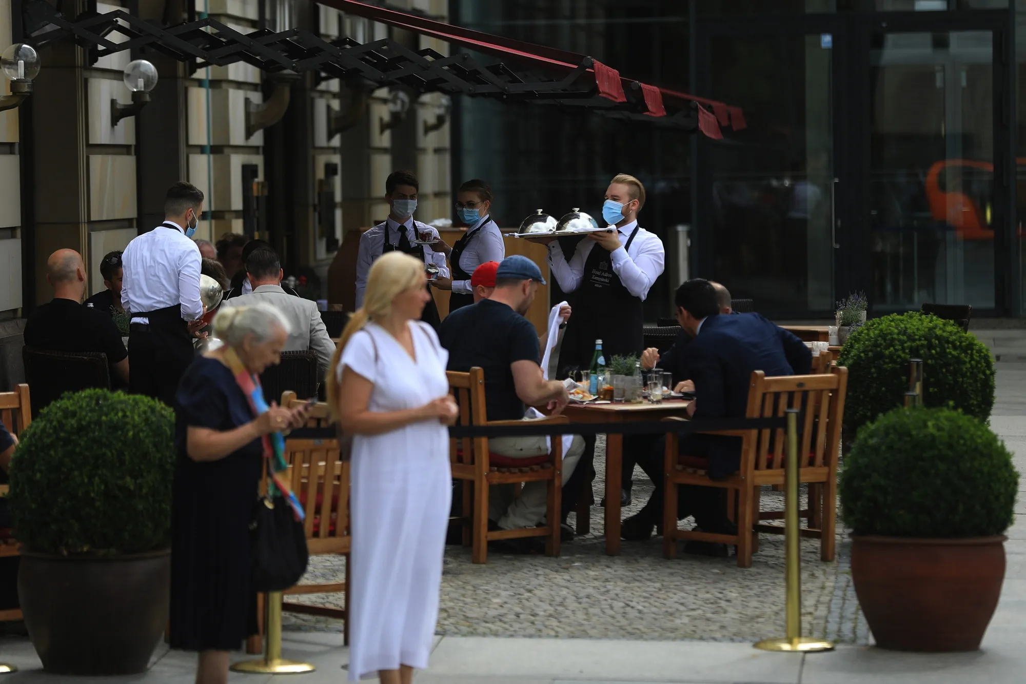 A waiter wearing a protective face mask serves customers at a restaurant terrace in Berlin.