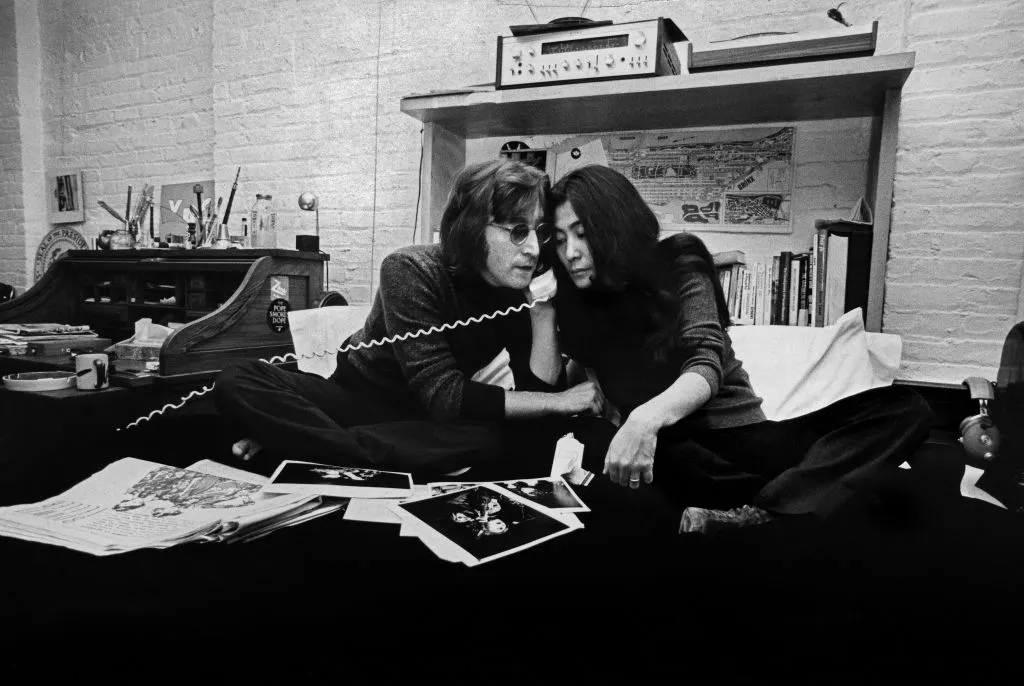 Jon and Yoko share a telephone receiver while seated on a bed in their West Village home.