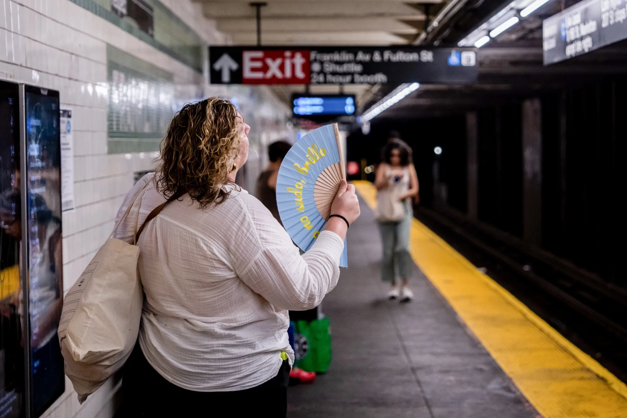 A commuter uses a hand fan at a subway station in New York.