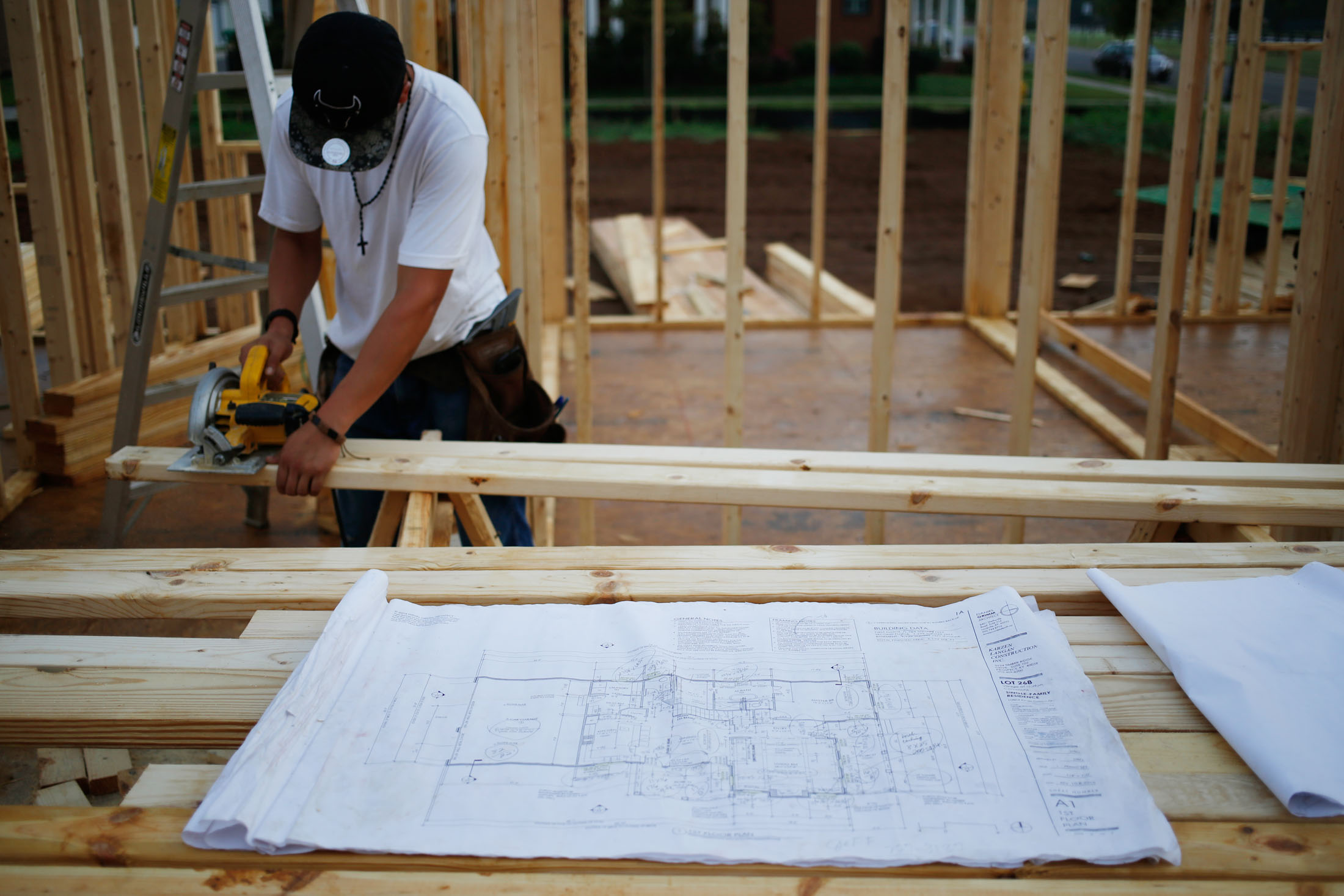 A set of blueprints sit in front of a contractor cutting lumber for a house under construction in Louisville, Kentucky.