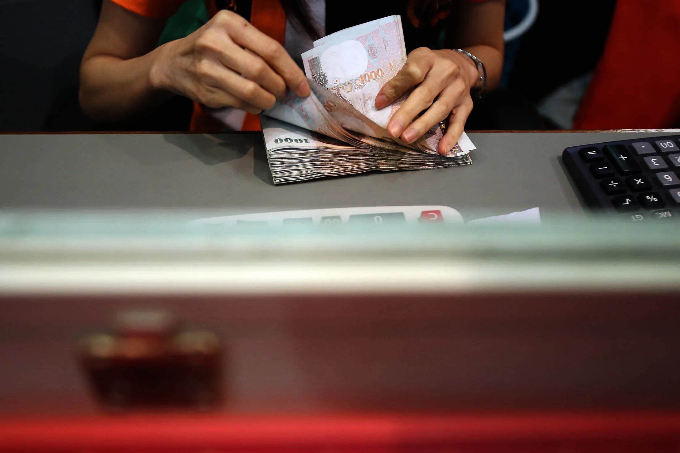 An employee counts one thousand Thai Baht banknotes at a branch of SuperRich money exchange shop in central Bangkok, on Thursday, August 22, 2013.
