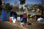 A homeless woman in Los Angeles stands with her dogs at her encampment. 