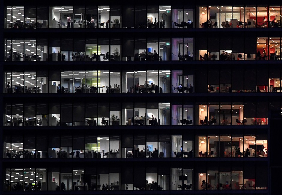 Workers in an office tower in London's Canary Wharf at dusk.