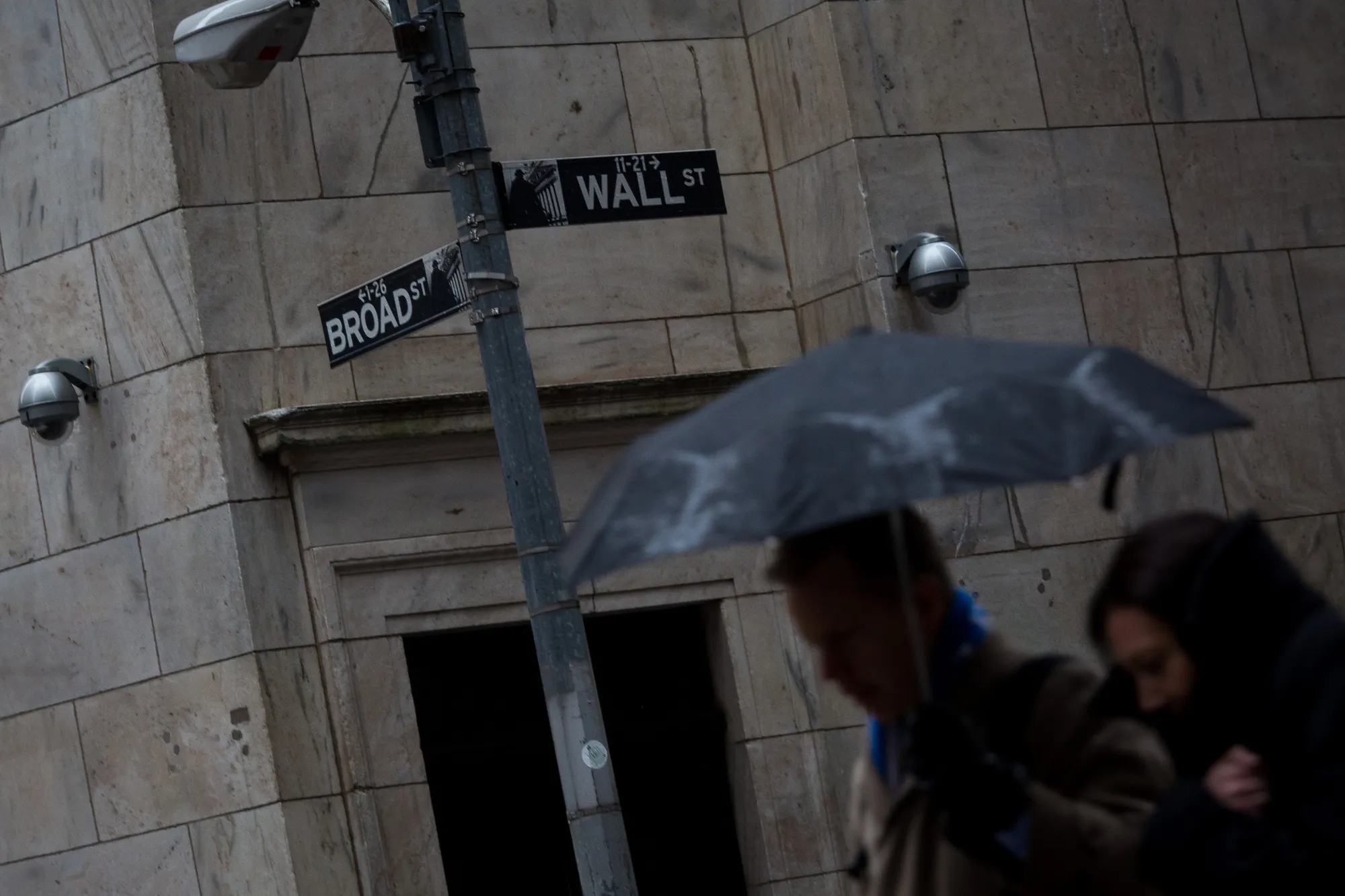 Pedestrians hold an umbrella in the rain while walking on Wall Street in New York