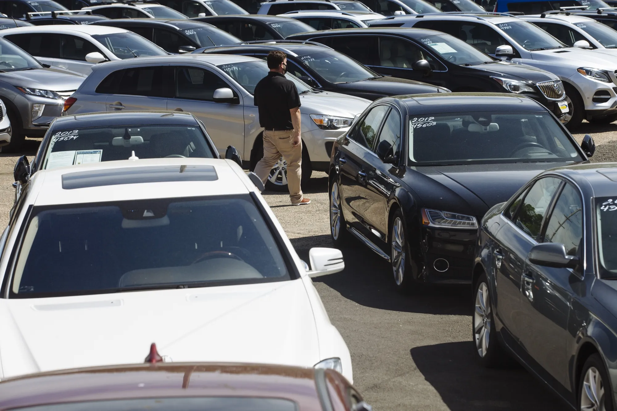 A car dealer walks past cars for sale at a used car dealership.