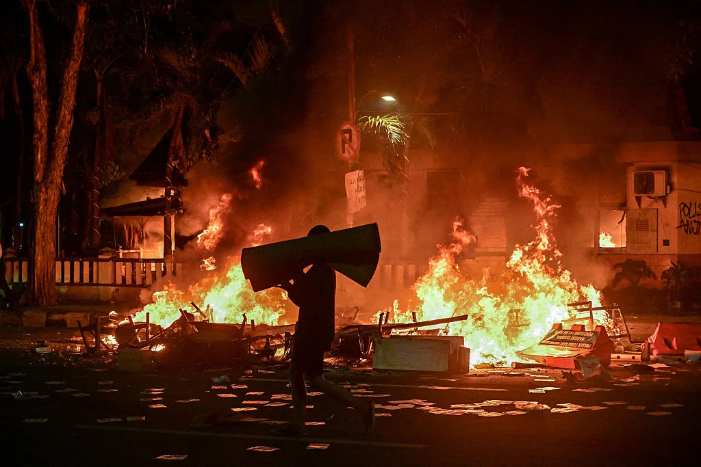 A protester carries looted goods in front of police headquarters that was set on fire, during demonstrations in Surabaya on Aug. 31.