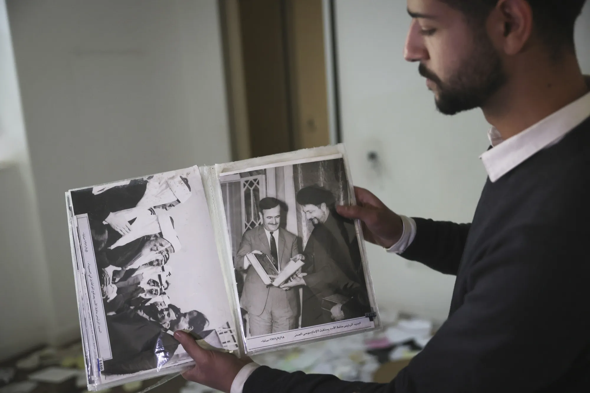 A man shows old pictures of the late Syrian President Hafez Assad, as people search for belongings in the ransacked residence of Bashar Assad, in Damascus.