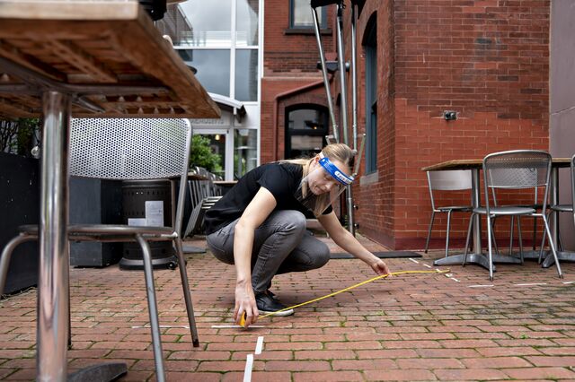 An employee wearing a protective shield uses a measuring tape to check the distance between tables and chairs in the outdoor seating area of a restaurant in Washington, D.C.