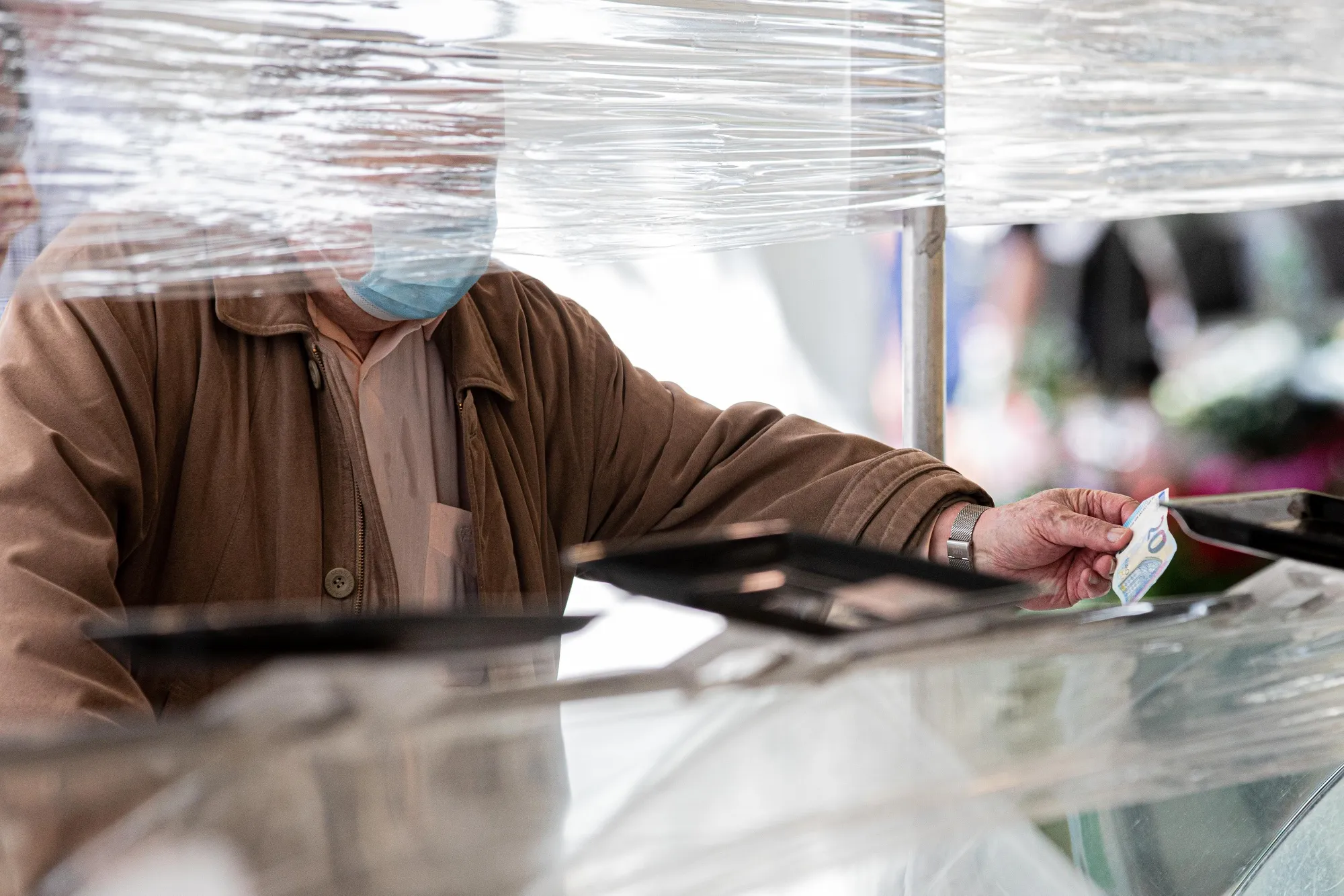 A customer wearing a protective face mask hands a ten euro banknote between protective cellophane screens on a fruit and vegetable market stall at Marche Saxe-Breteuil in Paris, on May 21.