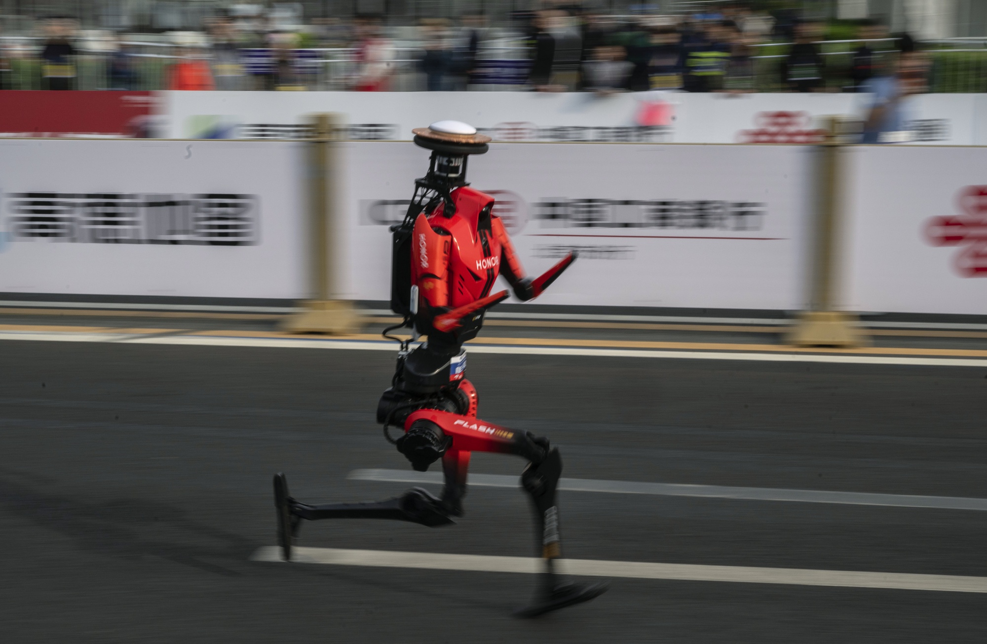 BEIJING, CHINA - APRIL 19: The fastest humanoid robot, an H1made by Honor, runs beside human runners at the start on its way to winning the Beijing Humanoid Half Marathon on April 19, 2026 in Beijing, China. The robot finished with a net time of 50 minutes and 26 seconds. More than 100 humanoid robots from 76 institutions across China lined up alongside 12,000 human runners Sunday in Beijing's E-Town district for the world's largest humanoid robot half-marathon, following the same 21-kilometre course on separate lanes in a 'human-robot co-running' format that for the first time included teams competing under fully autonomous navigation. (Photo by Kevin Frayer/Getty Images)
