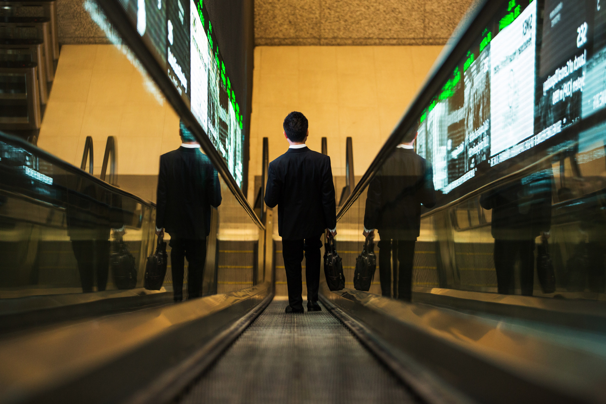 A man rides an escalator past an electronic screen at the Singapore Exchange Ltd.&nbsp;headquarters in Singapore.
