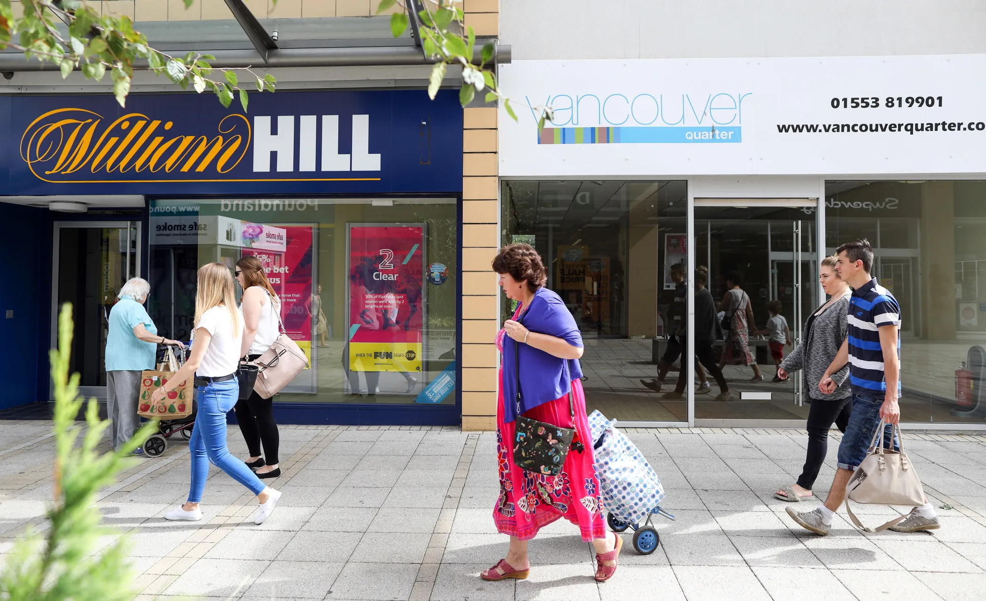Pedestrians pass a William Hill Plc betting shop&nbsp;at the&nbsp;Vancouver Quarter open-air mall in King's Lynn, U.K. on Aug. 29, 2017.