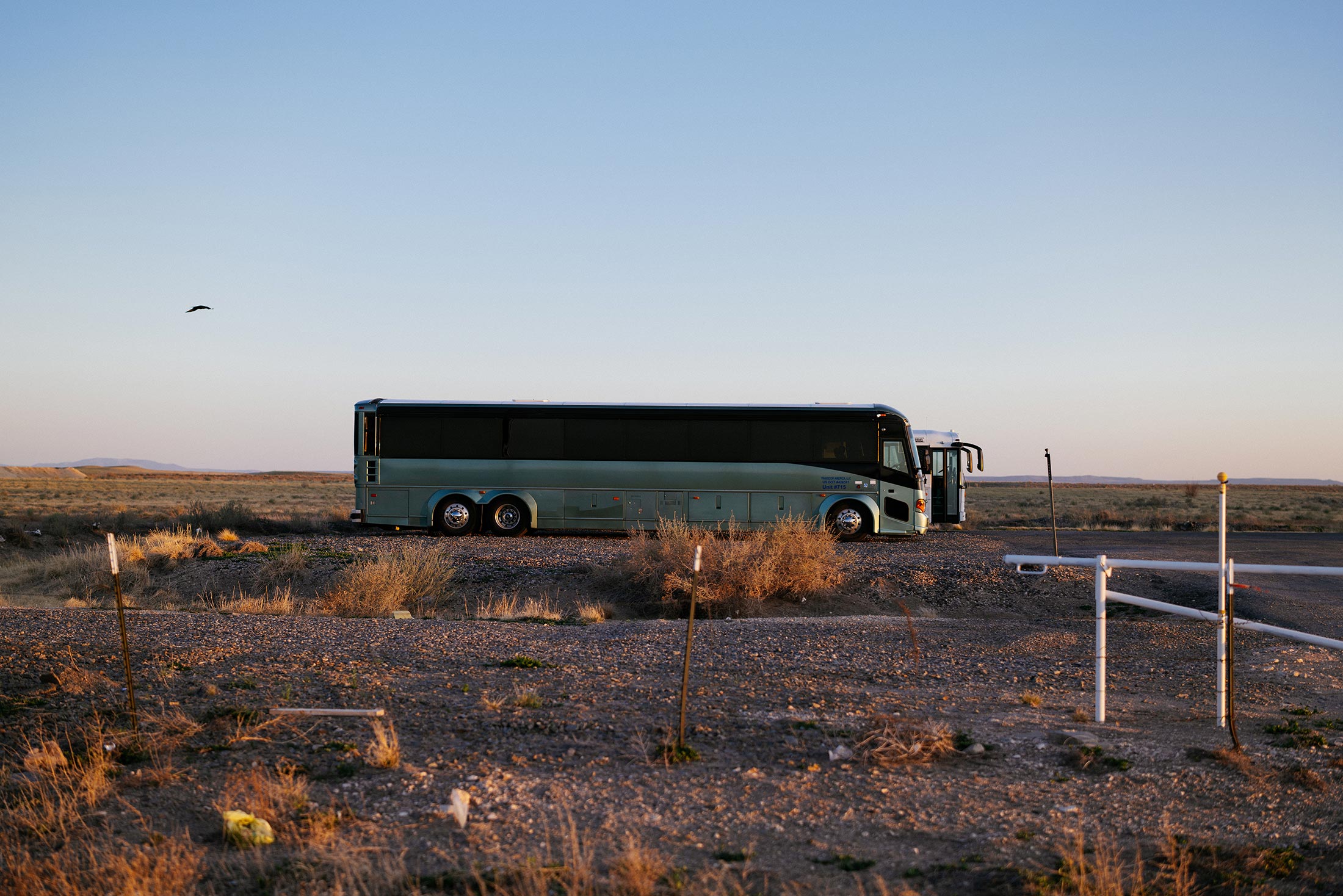 A green bus and a white bus are parked in an arid New Mexico setting on April 26, 2025.