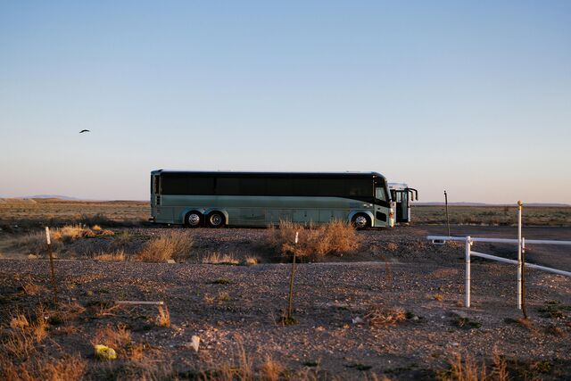 A green bus and a white bus are parked in an arid New Mexico setting on April 26, 2025.