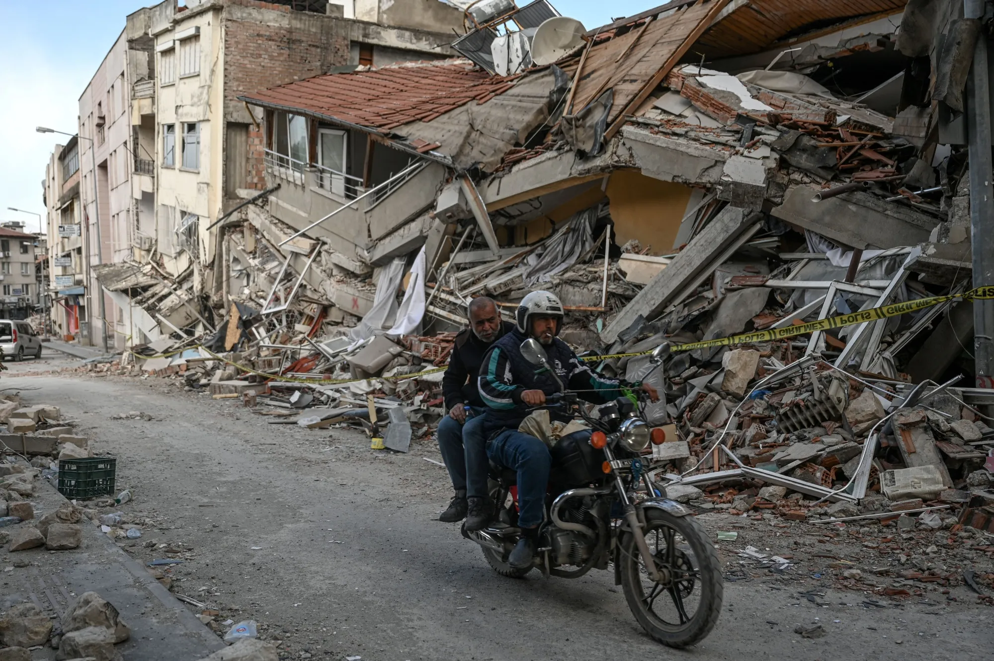 People ride a motorcycle next to the rubble of collapsed buildings in Hatay on March 6.