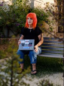 Micky Small sits on a bench outside with her laptop.