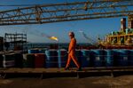 A worker passes stores of oil drums and gas flares while working aboard an offshore oil platform in the Persian Gulf's Salman Oil Field, operated by the National Iranian Offshore Oil Co., near Lavan island, Iran, on Friday, Jan. 6. 2017.&nbsp;