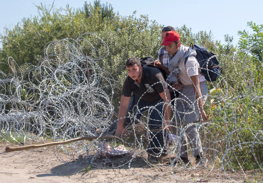 Migrants scramble through the border fence between Serbia and Hungary.
