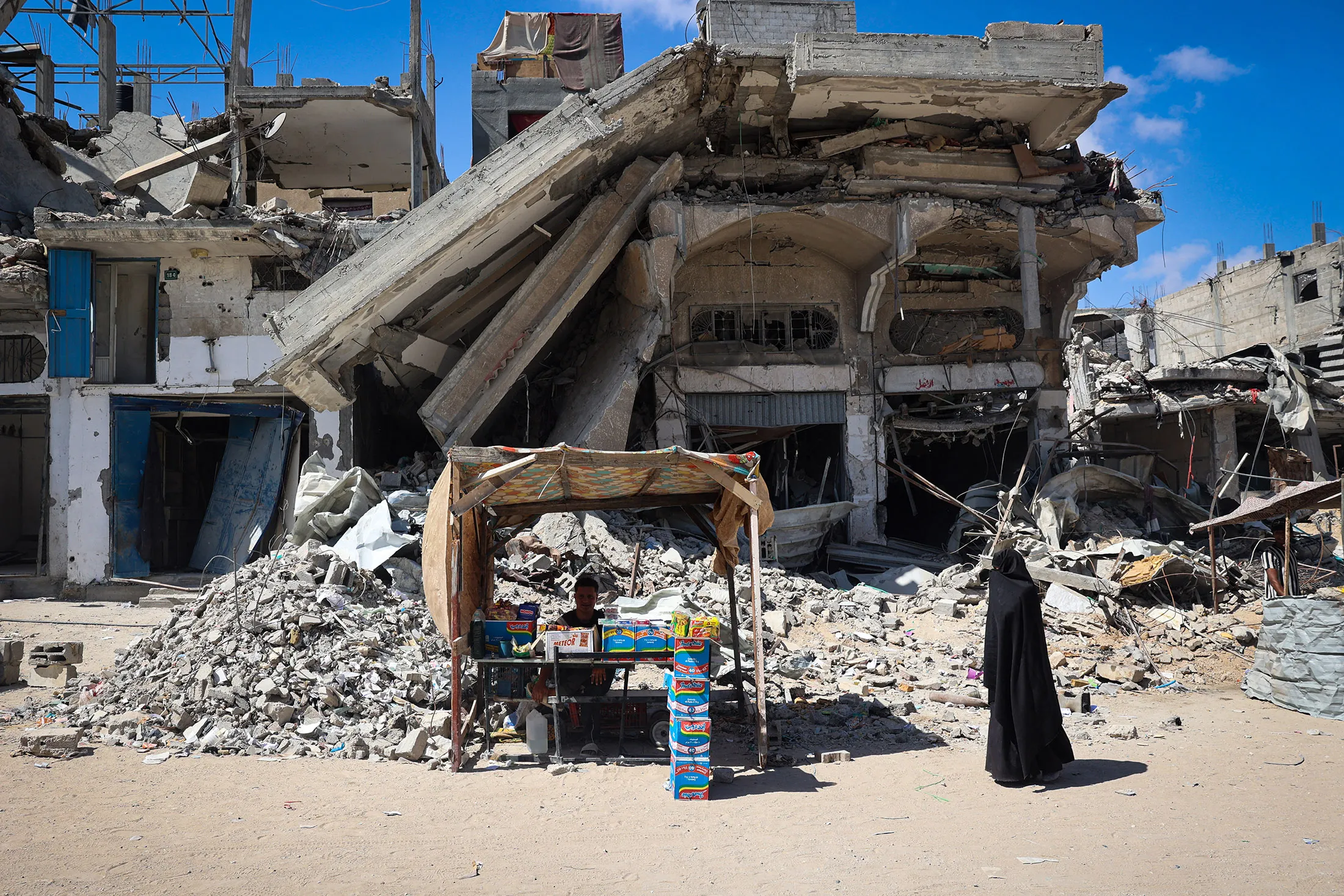 A displaced Palestinian man displays food items for sale in front of destroyed buildings in Khan Yunis in the southern Gaza Strip on May 24.