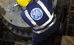 The company logo sits on an employee's overalls as he secures a metal cable to a section of a subsea oil and gas tree, at the General Electric Co. (GE) plant in Montrose, U.K.
