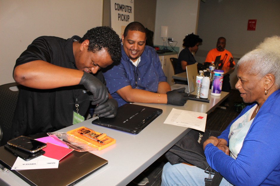 D.C. technicians Menelek Kebede (front) and Melehik Desta repairs a resident's computer during the first All Hands on Tech event, at the Anacostia Library.