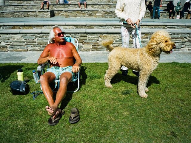 Starky the goldendoodle stands next to a very tan man sitting in a beach chair in Huntington Beach, California