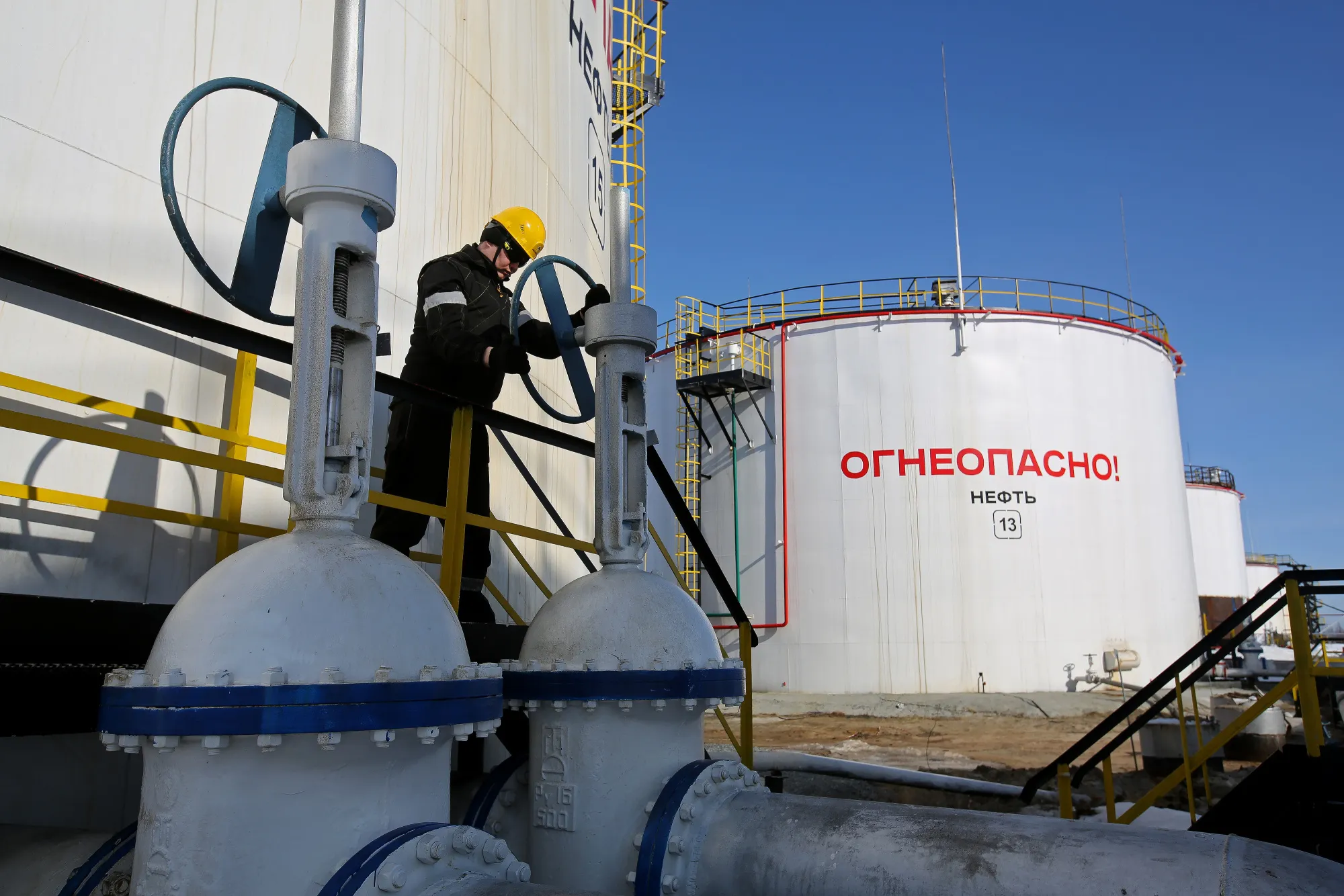 A worker turns a flow valve near oil storage tanks at a pumping station, operated by Rosneft PJSC, in the Samotlor oilfield near Nizhnevartovsk, Russia, on Monday, March 20, 2017. Russia's largest oil field, so far past its prime that it now pumps almost 20 times more water than crude, could be on the verge of gushing profits again for Rosneft PJSC.