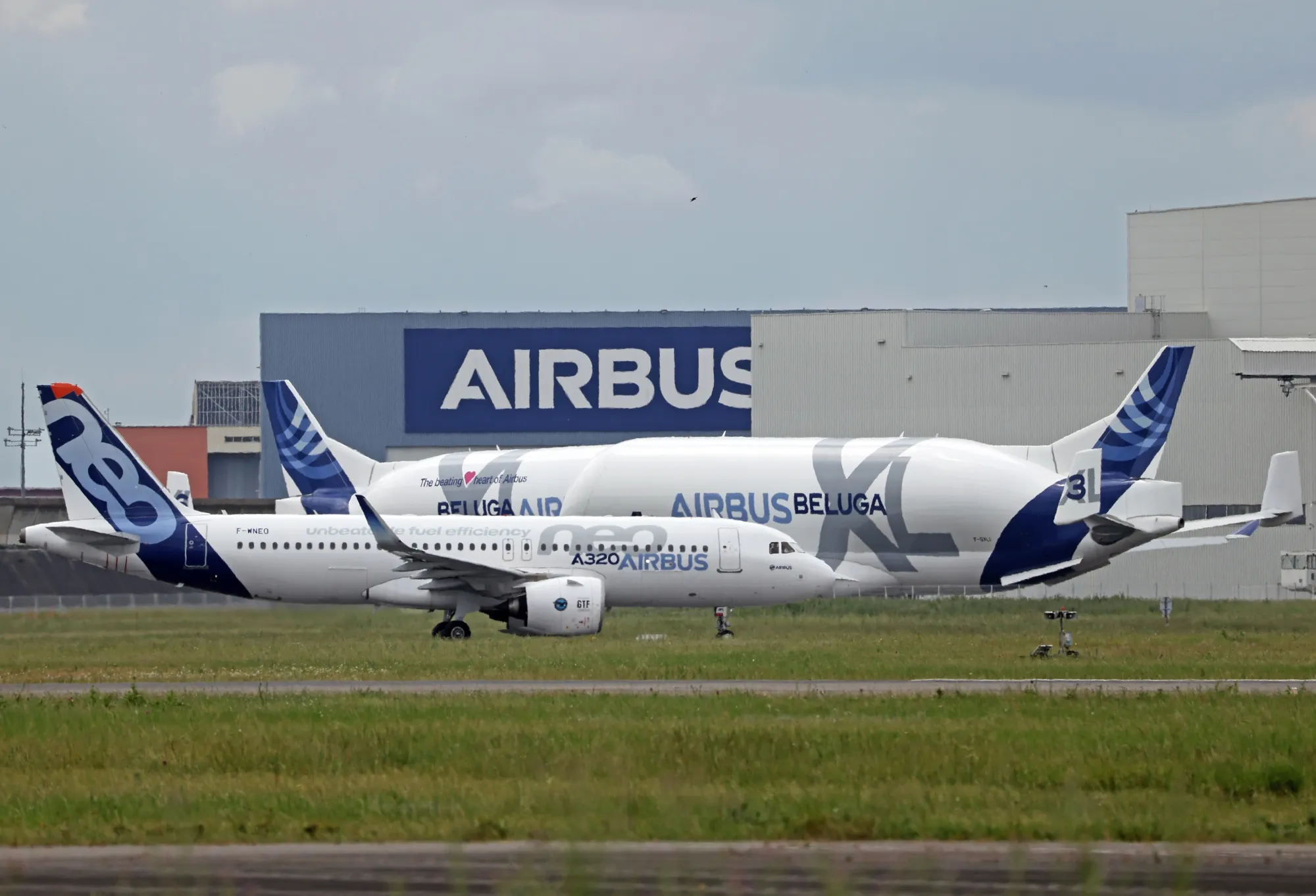 An Airbus A320neo, center front, near two Airbus Beluga aircraft in Toulouse Blagnac Airport.