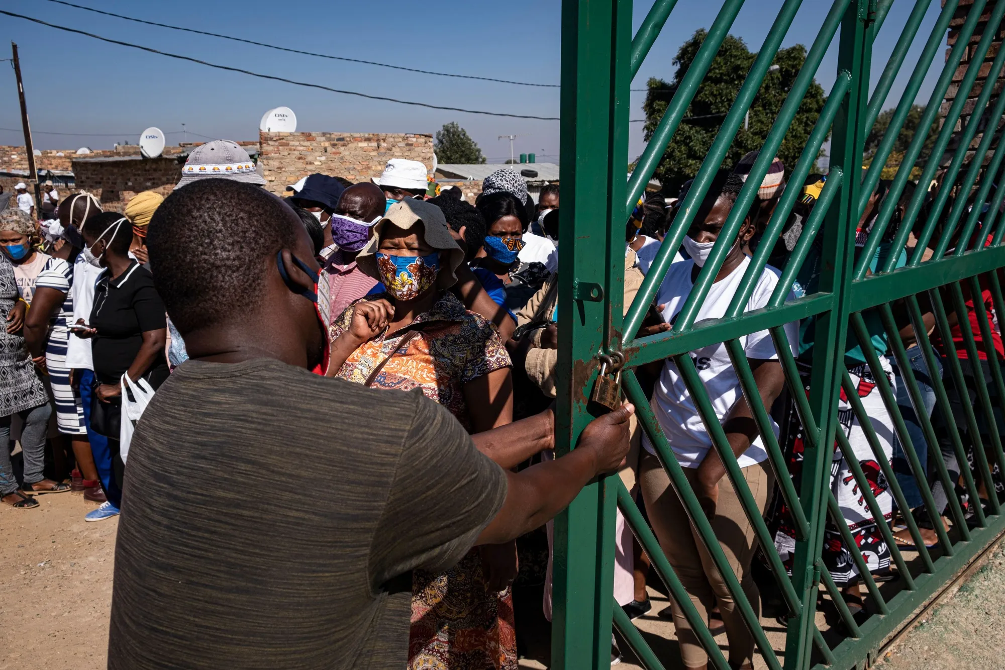 A person closes a gate leading to food parcels while residents look on during food distribution in Diepsloot, Johannesburg, on May 8.