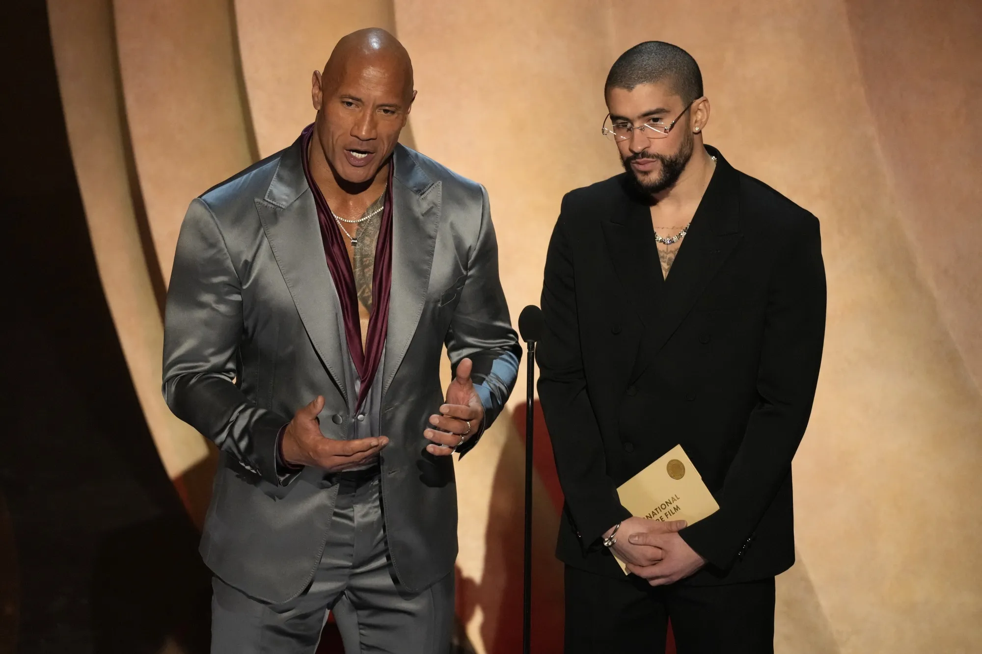 Dwayne Johnson, left, and Bad Bunny present the award for best international feature film during the Oscars on Sunday, March 10, 2024, at the Dolby Theatre in Los Angeles. (AP Photo/Chris Pizzello)