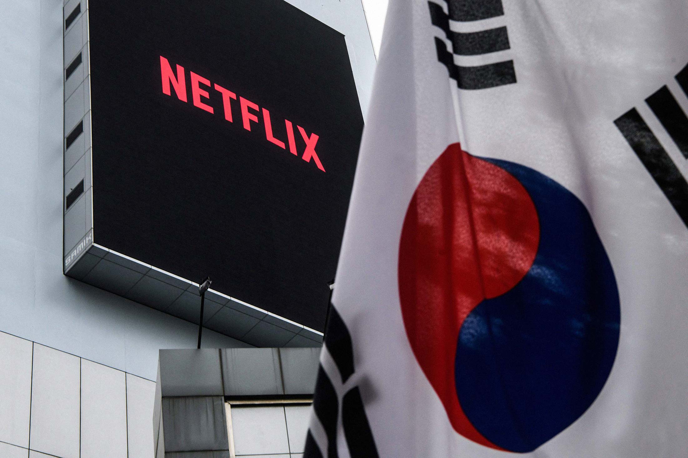 The logo of Netflix, producer of the hit series Squid Game, beyond a South Korean flag&nbsp;in Seoul.