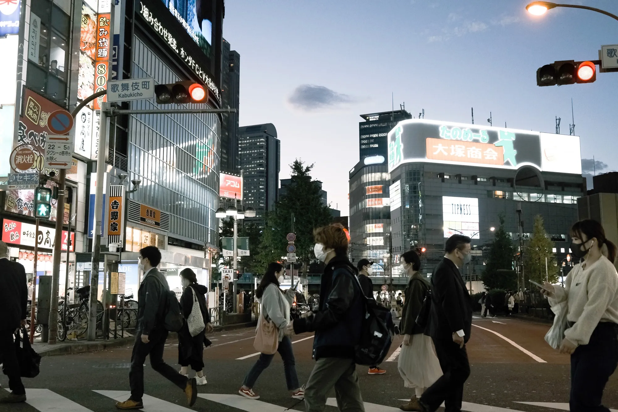 Pedestrians walk across a road at dusk in the Shinjuku district of Tokyo, Japan.
