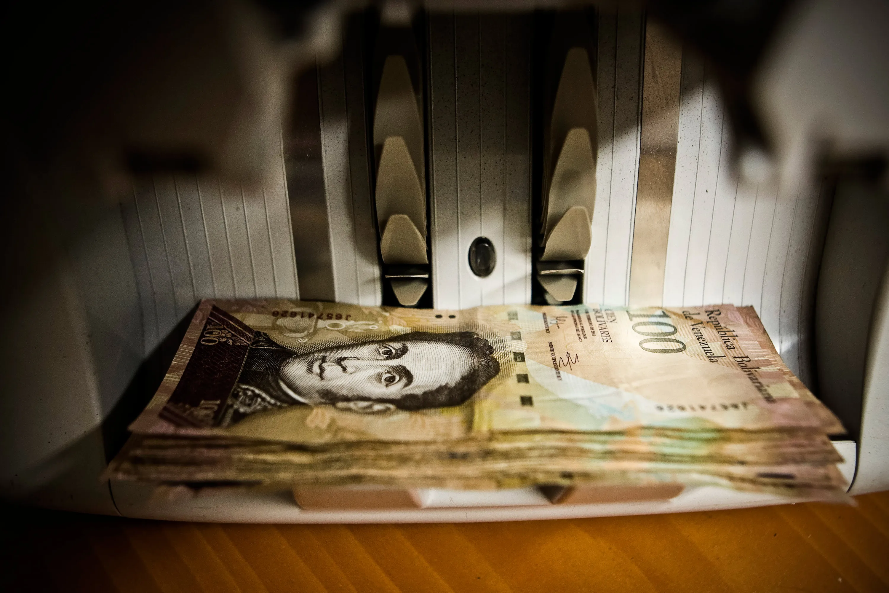 Bolivar notes are placed in a counting machine in this arranged photograph taken in Caracas, Venezuela, on Wednesday, Feb. 13, 2013.
