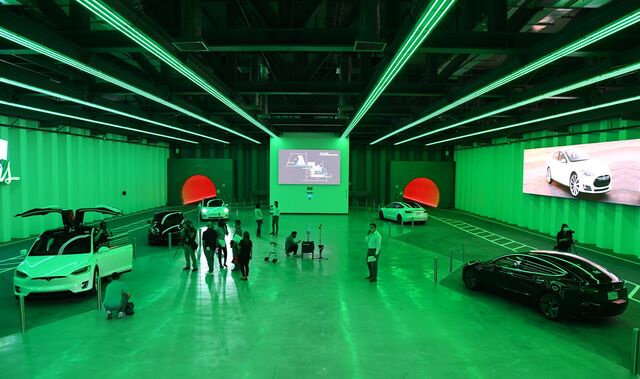 A photo of the Las Vegas loop station shows a large space bathed in green light, with four different cars parked at corners. The tunnels are filled with reddish light.